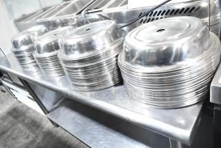 Stacks of metal dome covers on a stainless steel table. 98 pieces, shiny finish, used for food service.