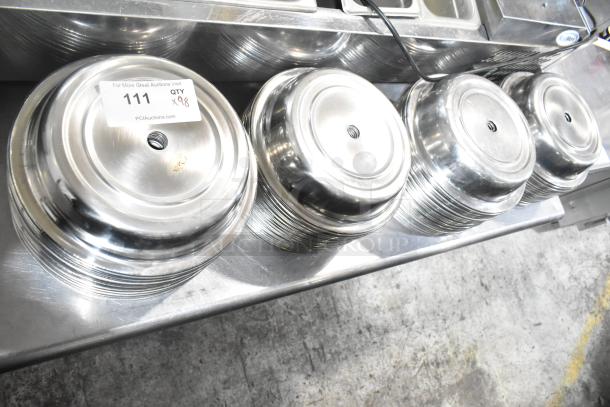 98 shiny metal dome covers stacked, marked with auction label 111, indicating quantity of 98, in excellent condition.