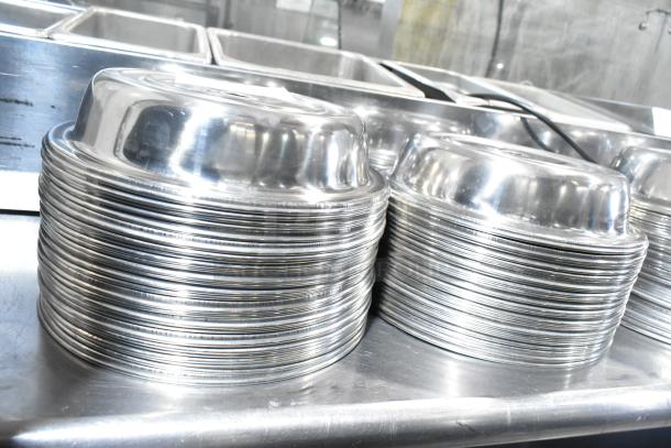 Stacks of 98 shiny metal dome covers in excellent condition on a stainless steel surface.