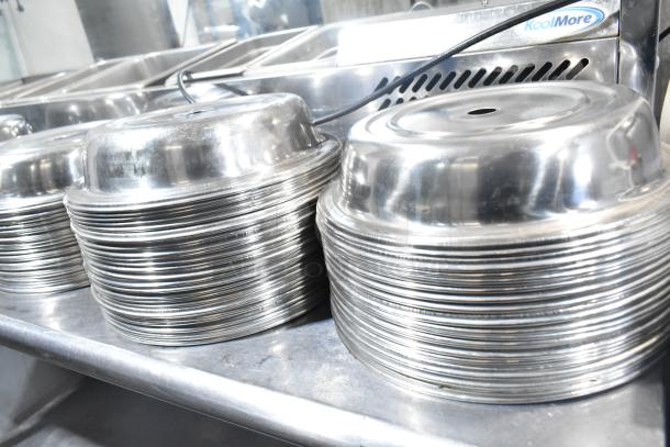 98 metal dome covers stacked on a table, shiny surface, suitable for food service, excellent condition.