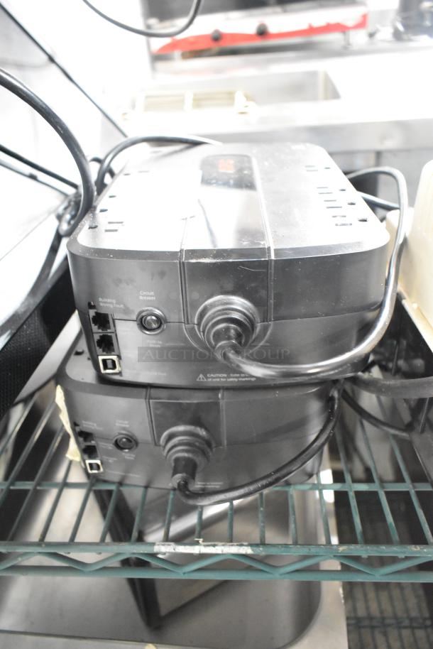 Two APC Uninterruptible Power Supplies with visible ports and power cables, placed on a shelf.