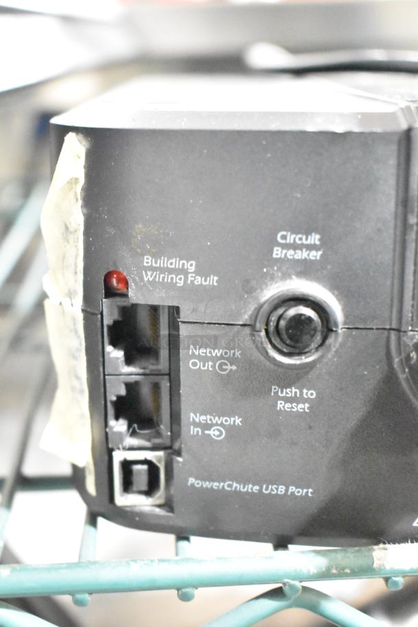 Close-up view of APC Uninterruptible Power Supply ports and indicators, featuring network in/out jacks and reset button.