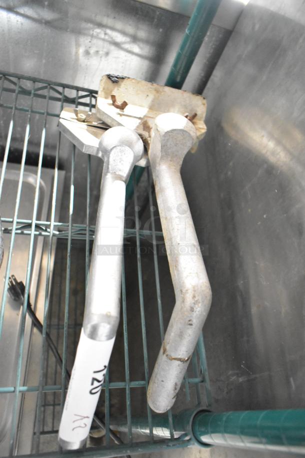 Two metal grill scrapers with long handles, showing signs of use. One scraper has a label with "120" and "2X" written on it.