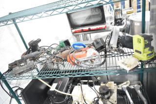 Assorted tools including angle grinder, Craftsman sander, Black and Decker sander/drill, Hitachi driver, Skilsaw saw on shelves.