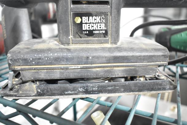 Black & Decker 1.6A finishing sander, visibly used, on a metal shelf. Label shows 15000 OPM. Part of an 8-item auction lot.