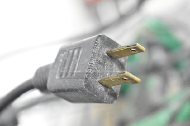 Close-up view of a two-prong electrical plug, part of a tool set auction with brands like Craftsman and Black and Decker.