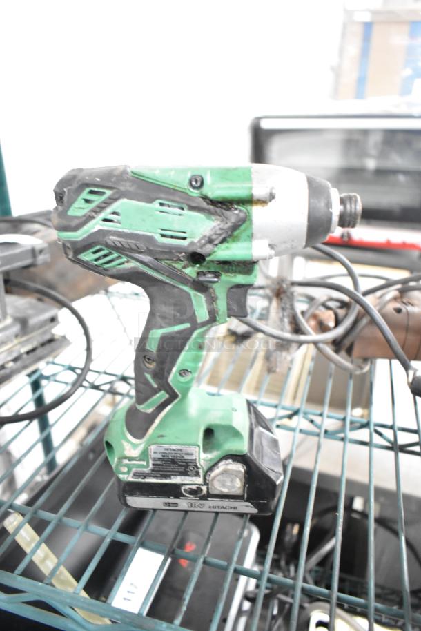 Hitachi cordless impact driver on metal shelf, in used condition. Visible markings indicate 18V model. Part of auction set.