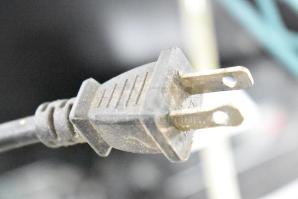 Close-up of a dusty power plug from a tool in a lot including an angle grinder, sanders, drill, impact driver, and saw.