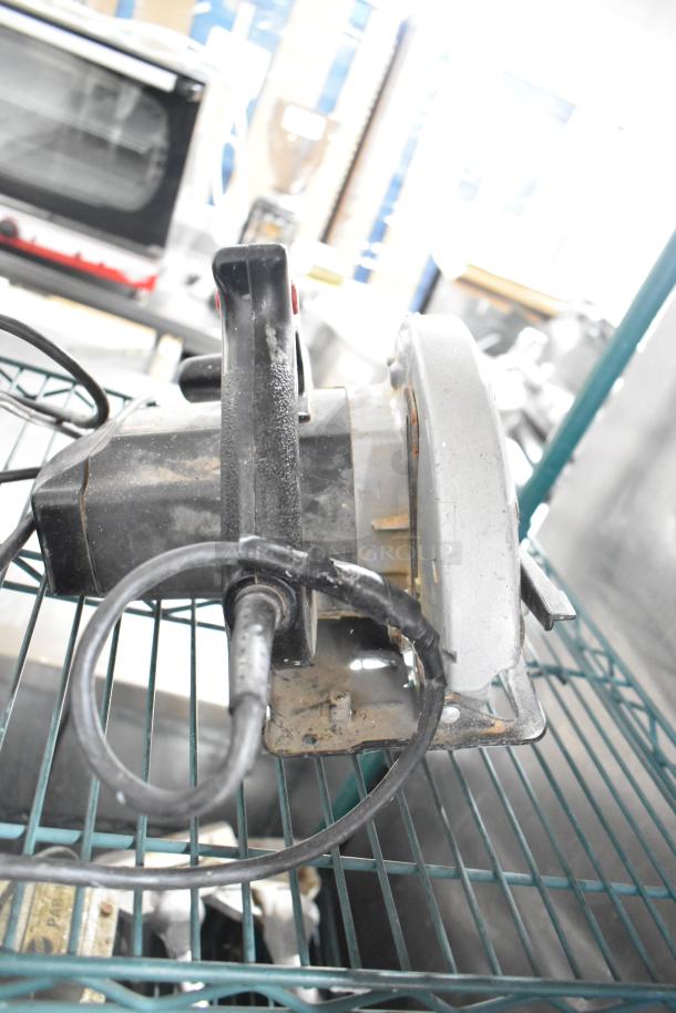 Angle grinder on wire shelf, displaying signs of wear. Part of a lot including sander, drill, impact driver, saw.