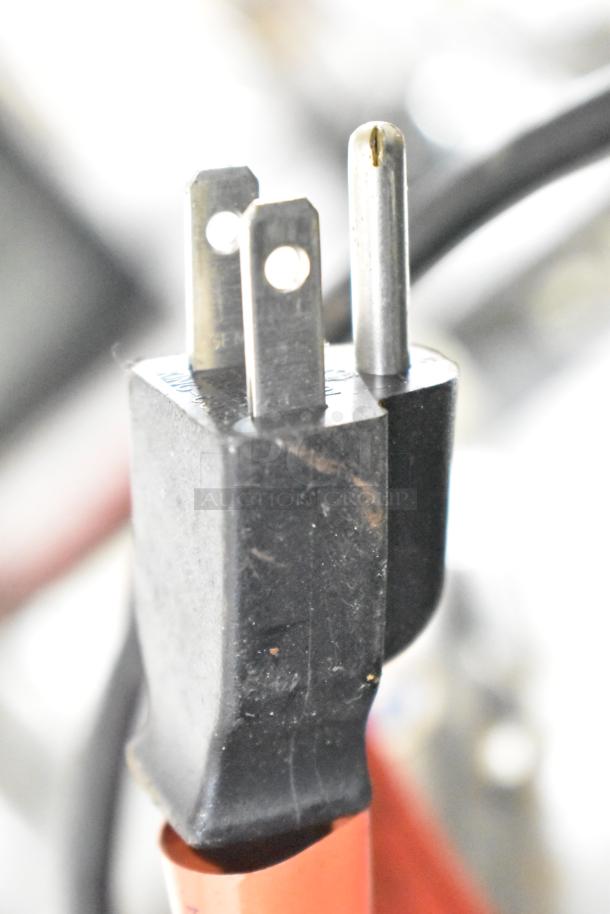 Close-up of a three-prong plug from a power tool, slightly worn, connected to a black cable.