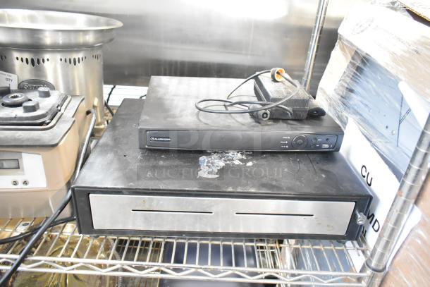 Alarmcom unit with cables and black cash drawer. Both items show signs of use. In working condition.
