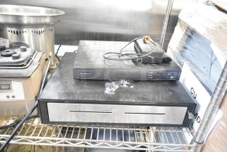 Alarmcom unit with cables and black cash drawer. Both items show signs of use. In working condition.