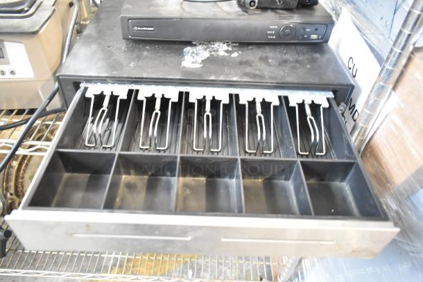Alarmcom unit and open cash drawer on shelf, both in used condition. Alarmcom branding visible on unit.