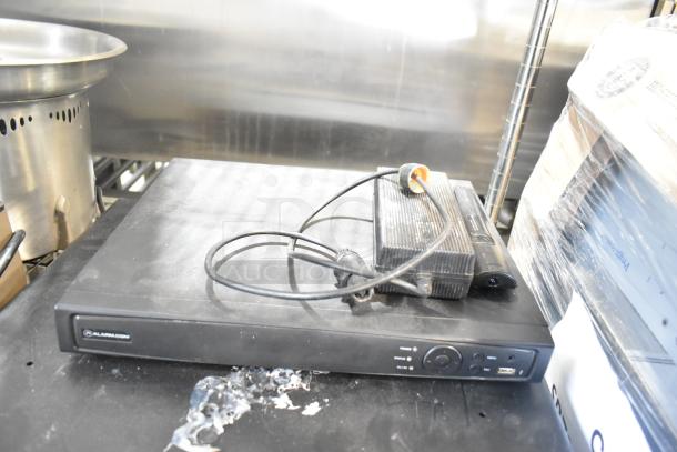 Alarmcom unit with cables on a black surface, showing power controls. Used condition. Part of a 2-item auction with a cash drawer.