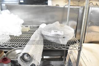 Brand new Lancaster Table & Seating stanchion, wrapped in bubble wrap with visible scratch and dent label, on metal shelf.