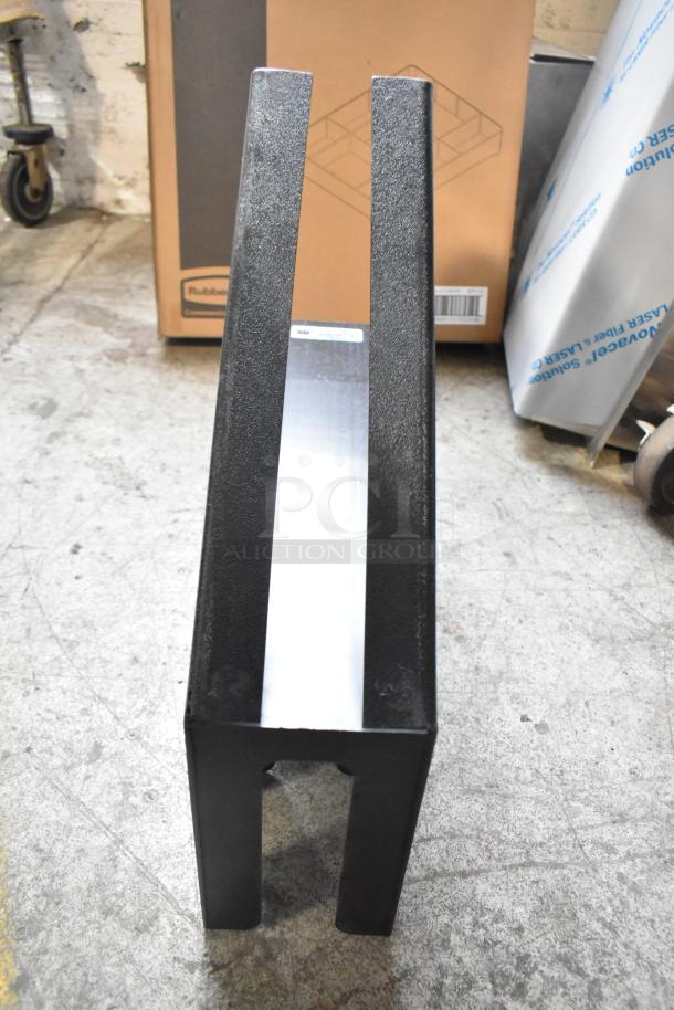 Black lid dispenser with textured finish, rectangular shape. Positioned on concrete floor. Boxes and materials in the background.