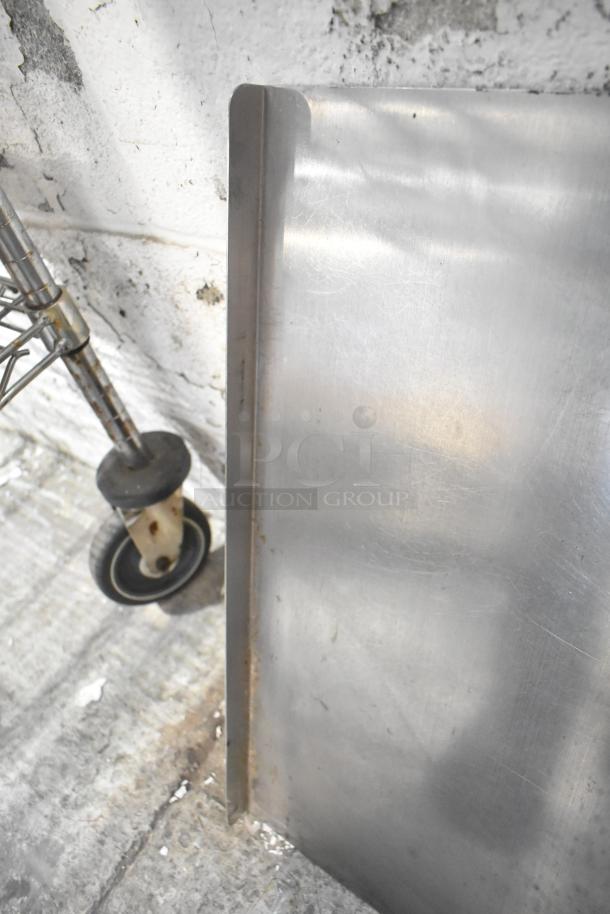 Alt text: Metal sheet with visible scuffs and wear next to a caster wheel from a blue poly rack. Auction item lot detail.