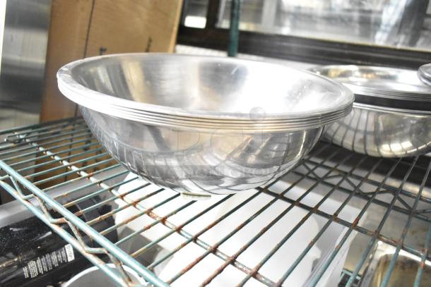 Set of 25 various metal bowls in used condition on a metal rack, reflective finish, great for culinary use.