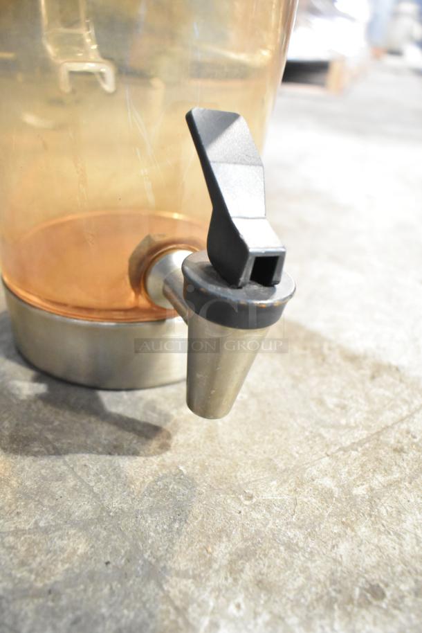 Beverage dispenser with metal spigot, semi-transparent container, and stainless base on concrete surface; good condition.