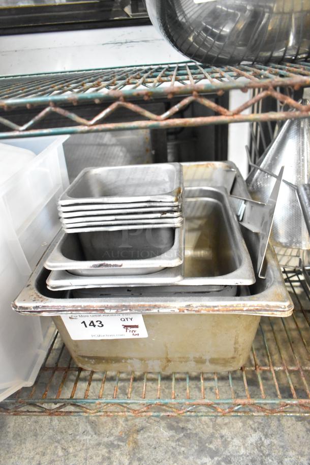 "Tiered lot of stainless steel drop-in bins and trays, includes various sizes. Visible rust and wear on edges. Auction tag #143."