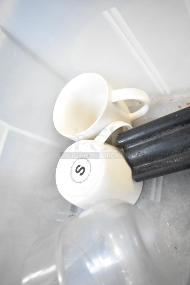 Various items including two white mugs, one with a Starbucks label, and a black cylindrical object in a bin.