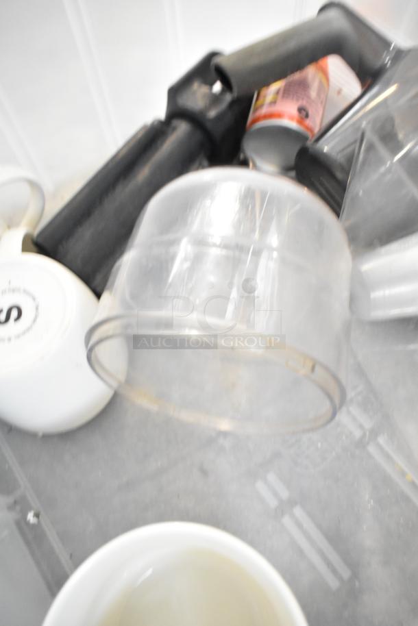 Auction lot with various items including a clear plastic drop-in bin, white mugs, and a beverage dispenser. Mixed condition.