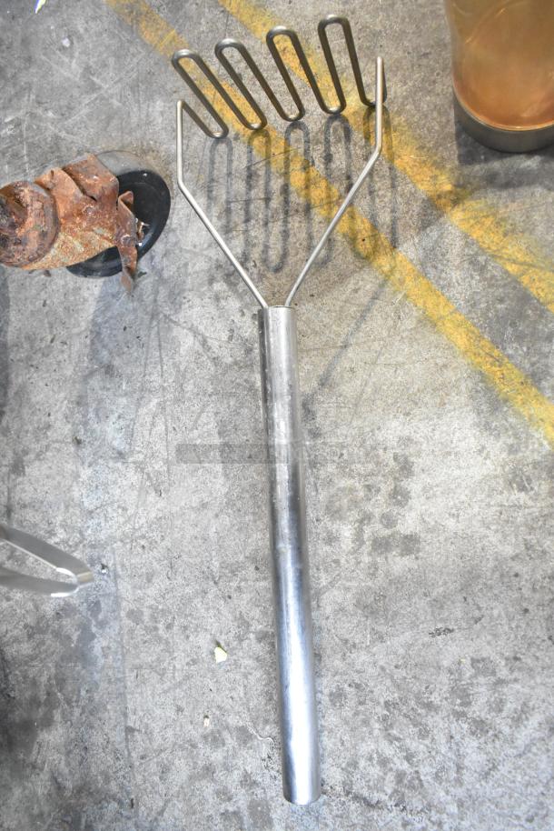 Metal rake-like tool with a stainless steel handle on concrete floor, showing signs of wear and rust.