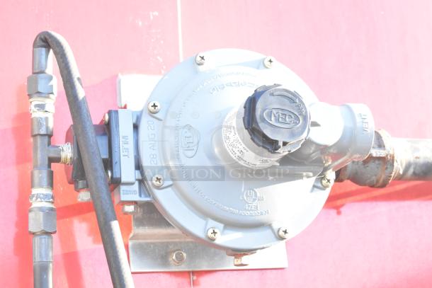 Close-up of MEC gas regulator on a red Titanium Cargo mobile kitchen trailer. Features inlet and vent markings.