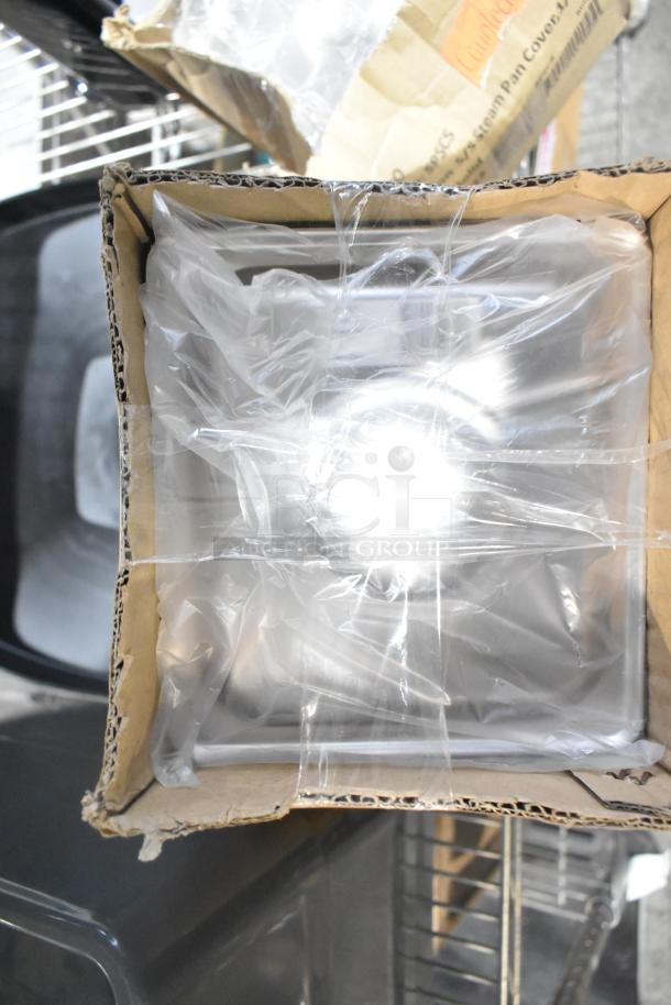 Cardboard box containing new SPSCS Winco steam pan lids, wrapped in plastic. Visible in storage with Slim Jim trash can lids.