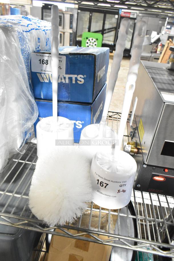 Four cleaning brushes including three toilet brushes and one cleaning brush, placed on a metal shelf, with auction labels indicating lot numbers.