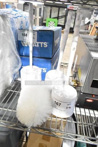 Four cleaning brushes including three toilet brushes and one cleaning brush, placed on a metal shelf, with auction labels indicating lot numbers.