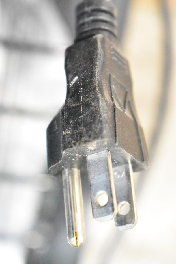 Close-up of a standard three-prong power plug, detail of electrical component, black plastic with metal prongs.