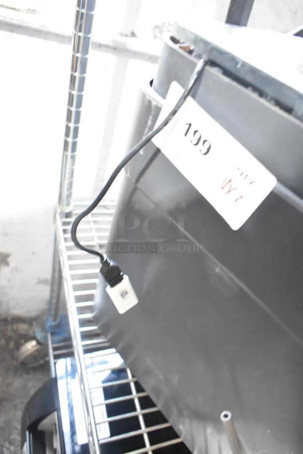 Two various fans, including Midea, with visible power cord and label displaying '199 QTY VX2', stored on metal shelf.