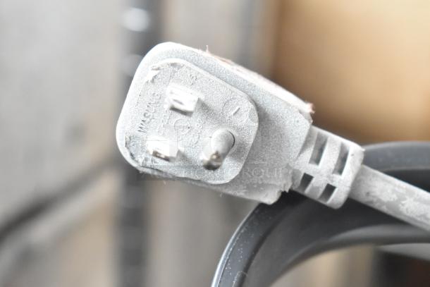 Close-up of a dusty three-pronged electrical plug attached to a fan, with "Midea" imprint visible on the plug.