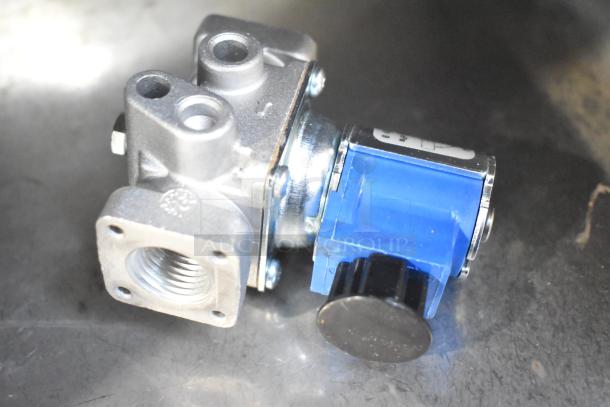 Close-up of a metal valve component with a blue housing and black knob, seen from above on a reflective surface.