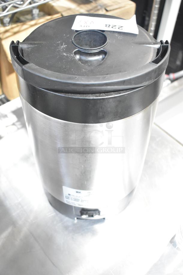 Stainless steel Hamilton Beach beverage dispenser with black top, shows wear, auction tag labeled "228," features spout and NSF mark.