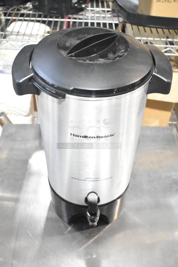 Hamilton Beach beverage dispenser, stainless steel, with black lid and spigot. Caution hot label visible. Good condition.