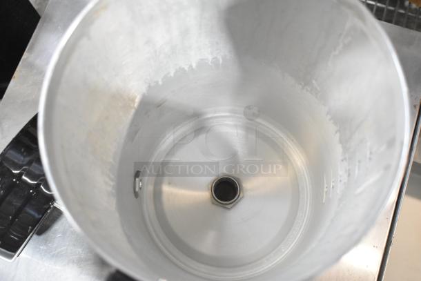 Interior view of a metal beverage dispenser, showing a slightly worn container and visible central drain hole.