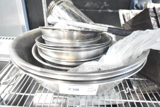Stack of metal bowls and containers on a wire shelf, labeled "230 QTY x18," indicating 18 items in used condition.