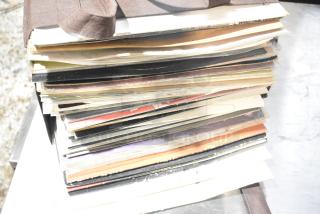 Stack of assorted vinyl records and items in a bundle. Some album covers show minor wear. Dark fabric strap visible.