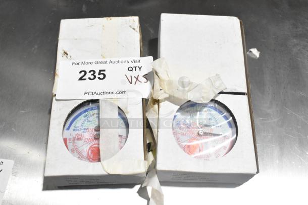Two boxed pressure gauges labeled with auction lot number 235, quantity five, on a metal surface.