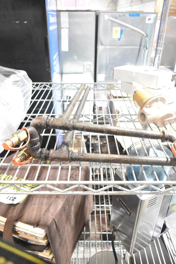 Five industrial items including a Watts unit, pipe with Ansul tips, gauges, all on a metal rack, showing signs of wear.