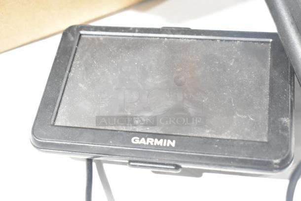 Dusty Garmin GPS unit, black frame, slightly worn, with visible power cable. Part of a lot including 3 GPS devices.