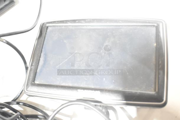 Alt text: TomTom GPS device with worn screen and visible scratches, surrounded by tangled cables.