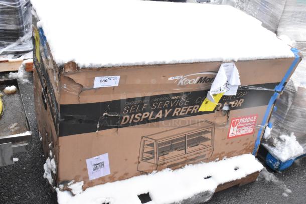 Boxed KoolMore CDC-250-WH self-service display refrigerator, snow-covered, with visible scratch and dent damage. Fragile label on box.