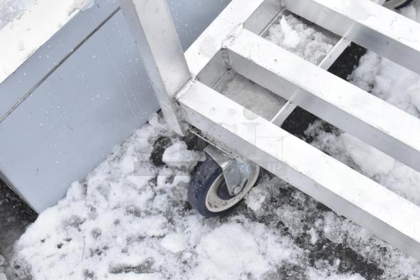 Metal dunnage-style cart with casters on snowy ground, showing sturdy metal slats and blue caster wheels.