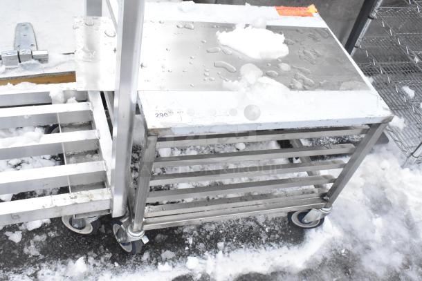 Commercial pan rack with stainless steel shelves and heavy-duty casters, shown outdoors with some snow on surfaces.