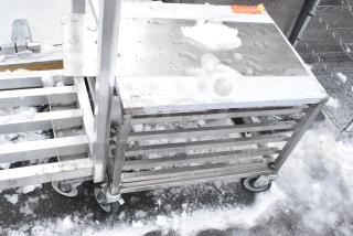 Commercial pan rack with stainless steel shelves and heavy-duty casters, shown outdoors with some snow on surfaces.