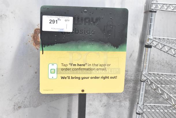 Weathered curbside pickup sign with QR code and instructions for order confirmation. Display rack visible beside it.