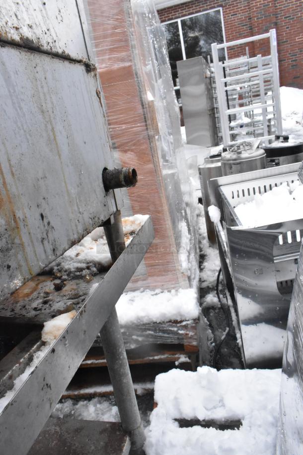 Commercial countertop charbroiler grill on equipment stand, visible rust and wear, outdoors in snowy conditions.